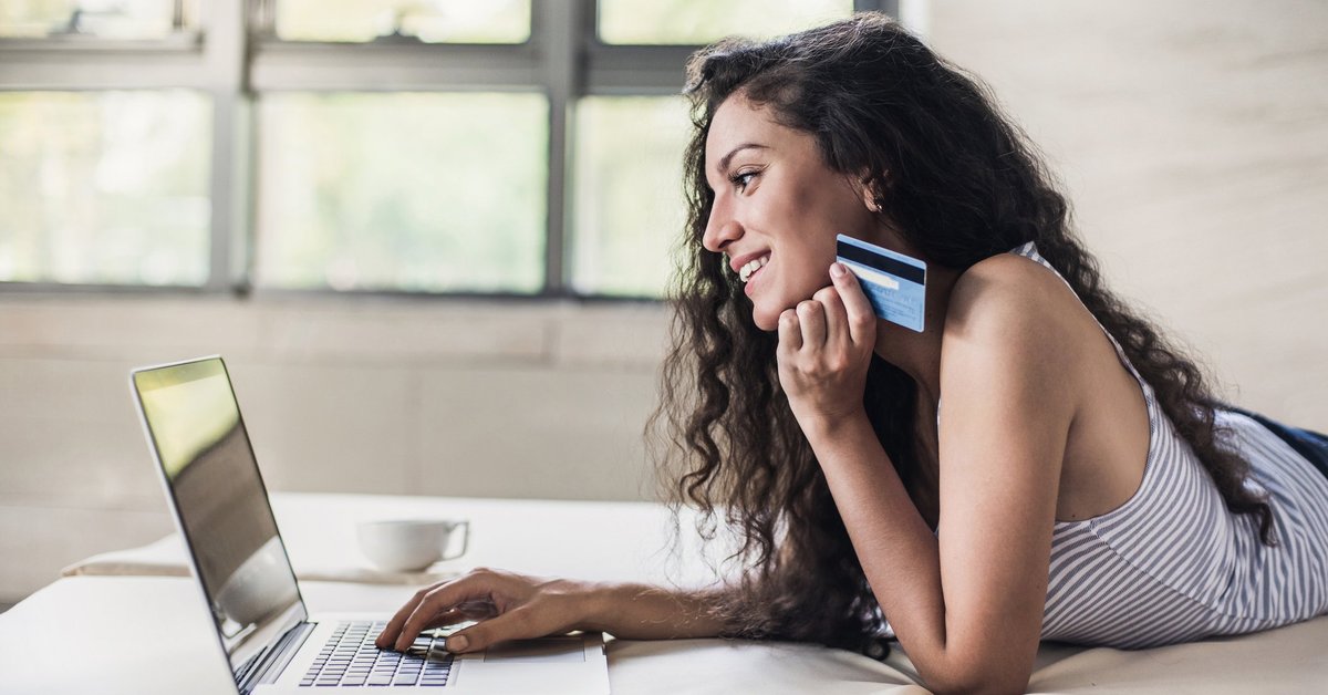 Young woman holding a credit card in her hand as she uses a laptop.