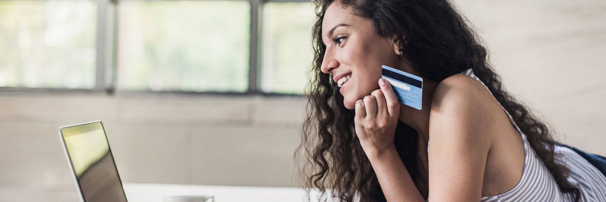 Young woman holding a credit card in her hand as she uses a laptop.