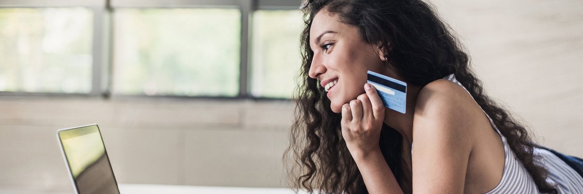 Young woman holding a credit card in her hand as she uses a laptop.