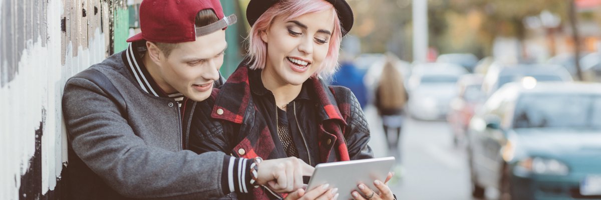 Two young adults outdoors smiling and pointing at tablet screen.