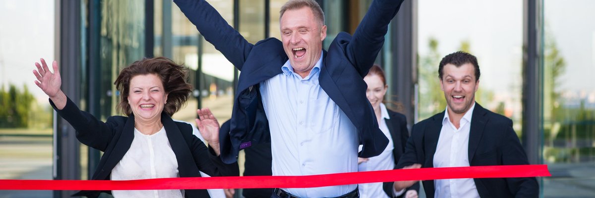Business people triumphantly running through red ribbon.
