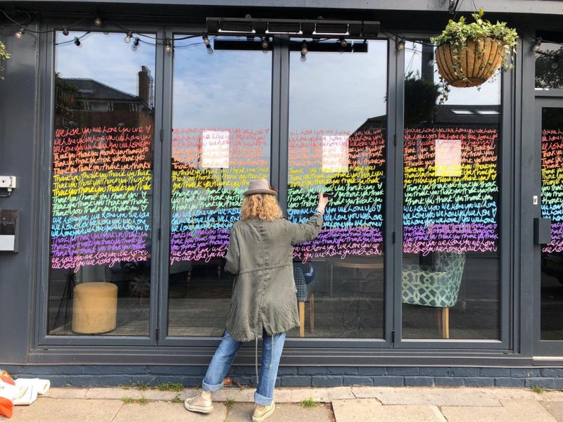Woman writing on a rainbow colored shop window.