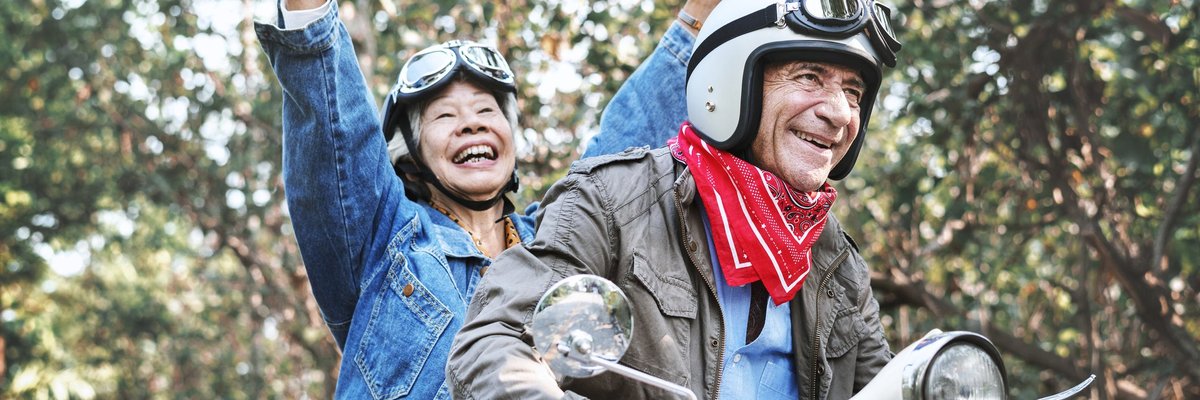 An older couple laughing while riding a moped.