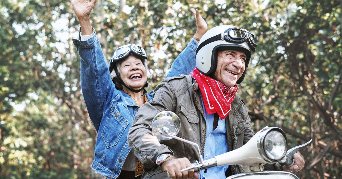 An older couple laughing while riding a moped.