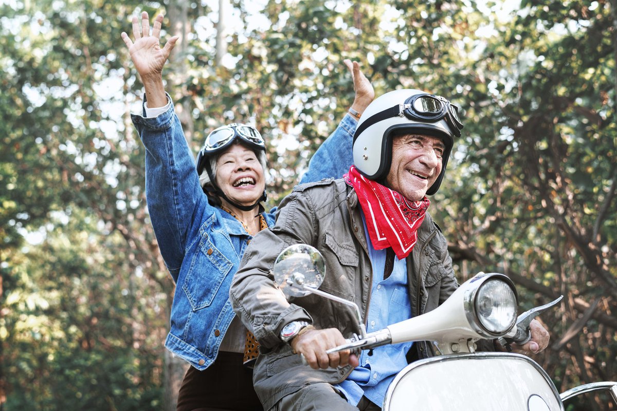 An older couple laughing while riding a moped.