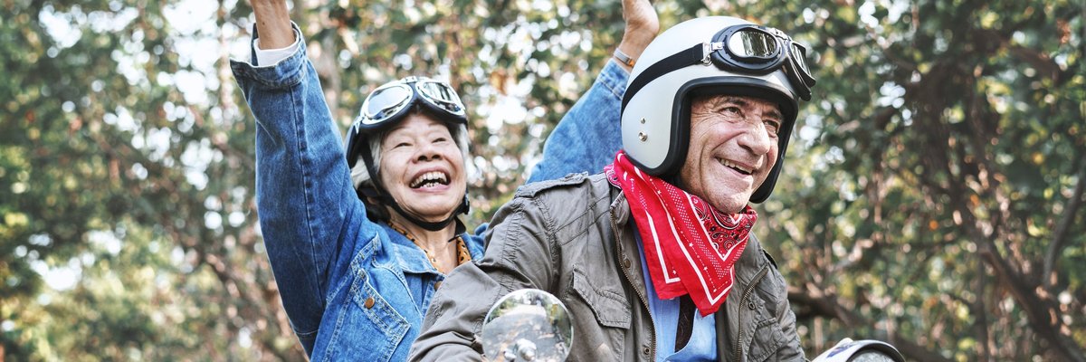 An older couple laughing while riding a moped.