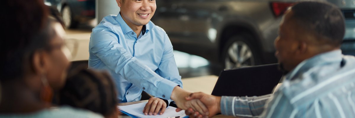 Salesman and customer shaking hands over paperwork at car dealership