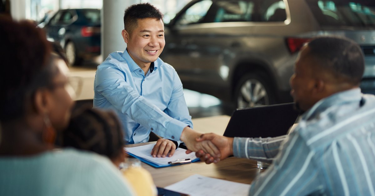 Salesman and customer shaking hands over paperwork at car dealership