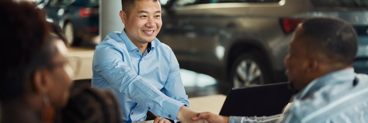 Salesman and customer shaking hands over paperwork at car dealership