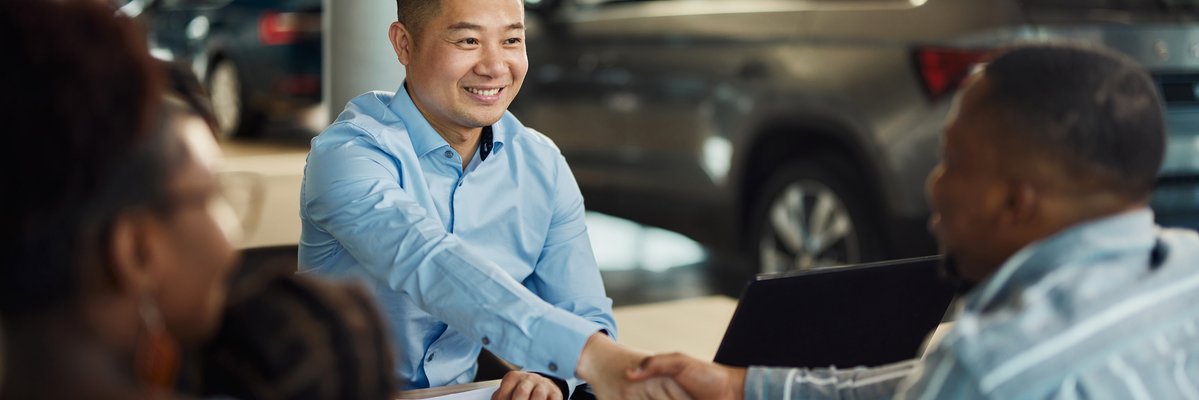 Salesman and customer shaking hands over paperwork at car dealership