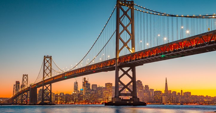 A view of San Francisco at sunset from across the water with the Bay Bridge in the foreground.