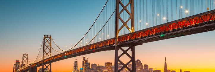 A view of San Francisco at sunset from across the water with the Bay Bridge in the foreground.