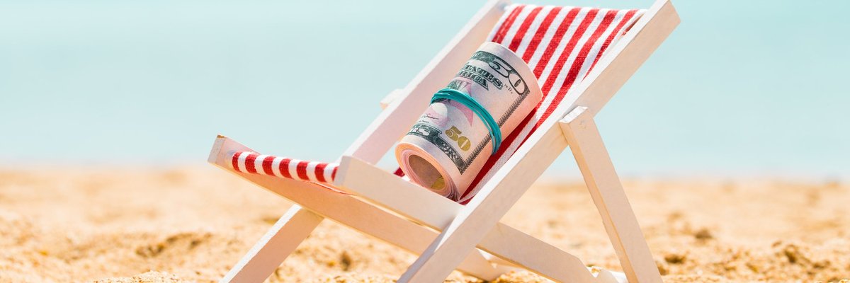 Rolled-up wad of cash placed in small beach chair on a sandy beach.