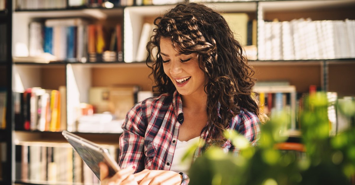 Smiling Young Woman Using Tablet In Library