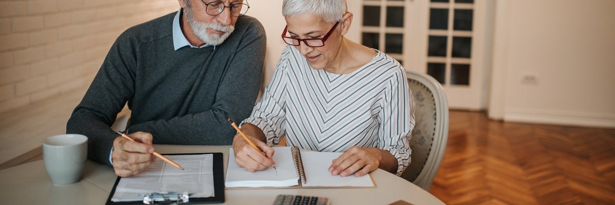 Senior couple analyzing expenses using a notebook and calculator.