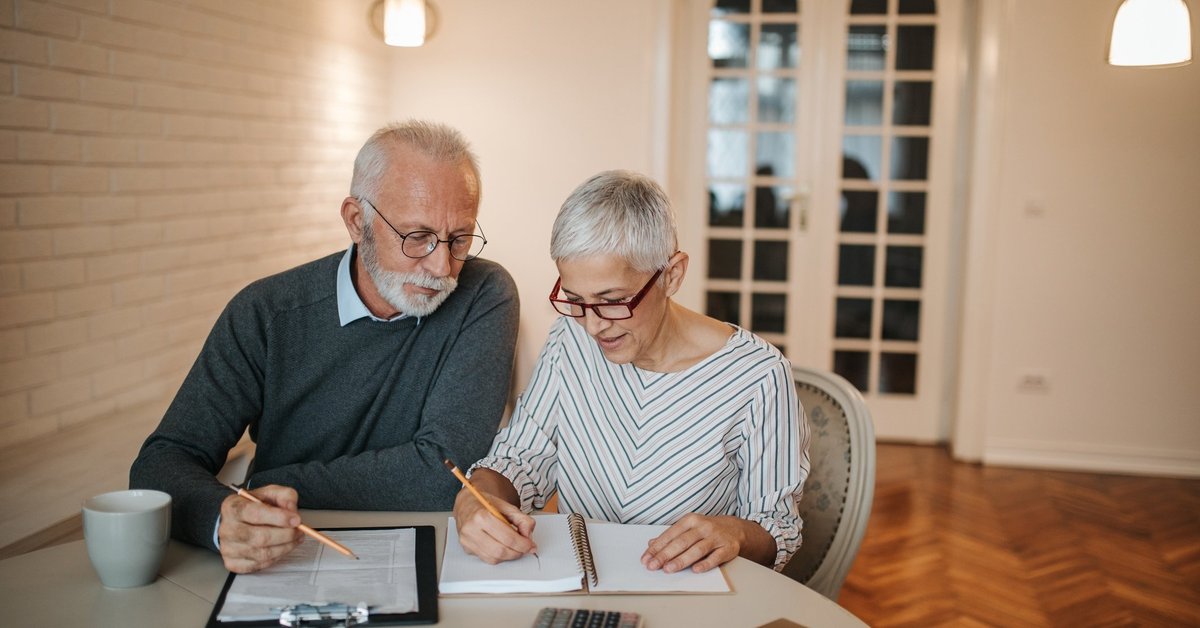 Senior couple analyzing expenses using a notebook and calculator.