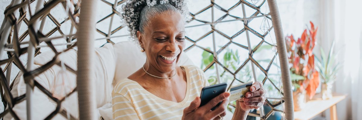 Senior woman holding a credit card and her cell phone smiling.