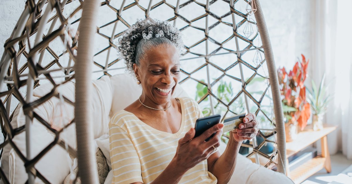 Senior woman holding a credit card and her cell phone smiling.