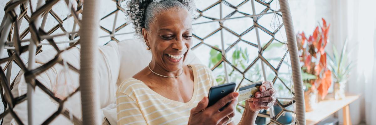 Senior woman holding a credit card and her cell phone smiling.