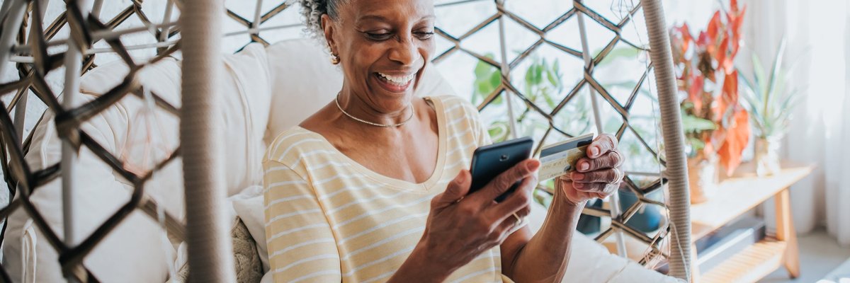 Senior woman holding a credit card and her cell phone smiling.
