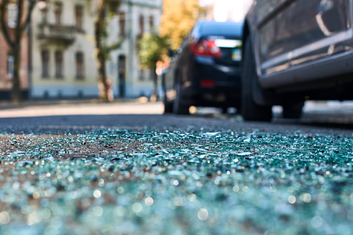 Shattered glass on a street next to parked cars.