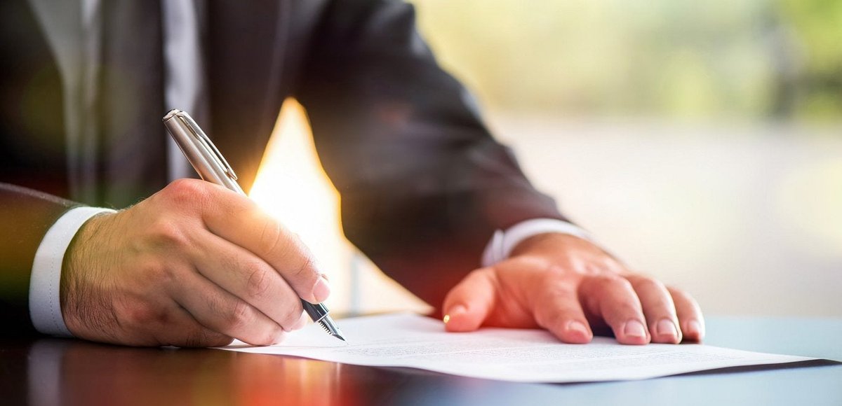Man in business suit signing his signature on a piece of paper.