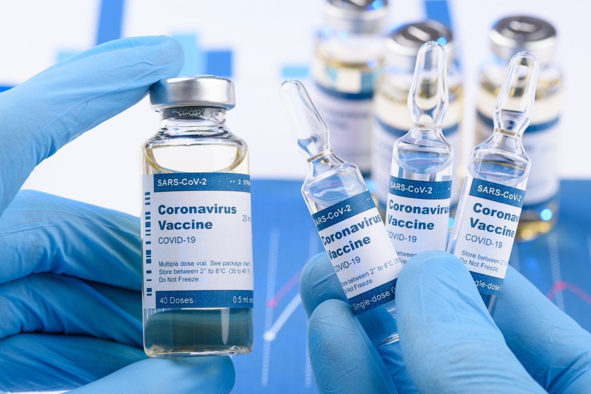 Medical worker with blue gloves holding vials labeled Coronavirus Vaccine.