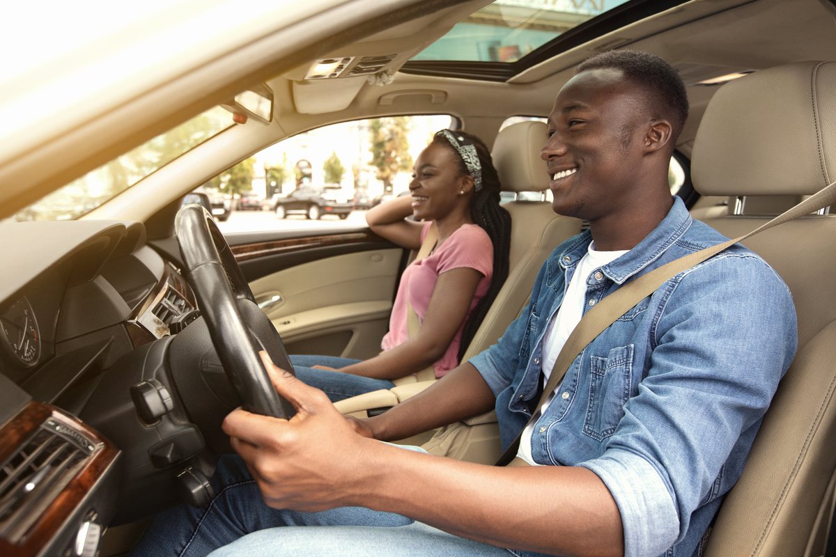 A smiling couple are in a car, enjoying the sunny day.