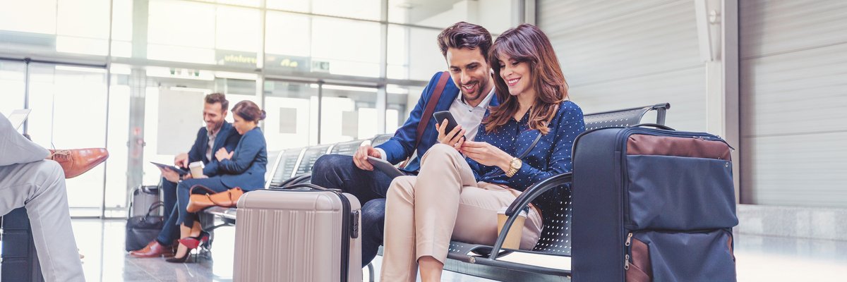 Smiling couple looks at phone together while waiting with luggage in airport