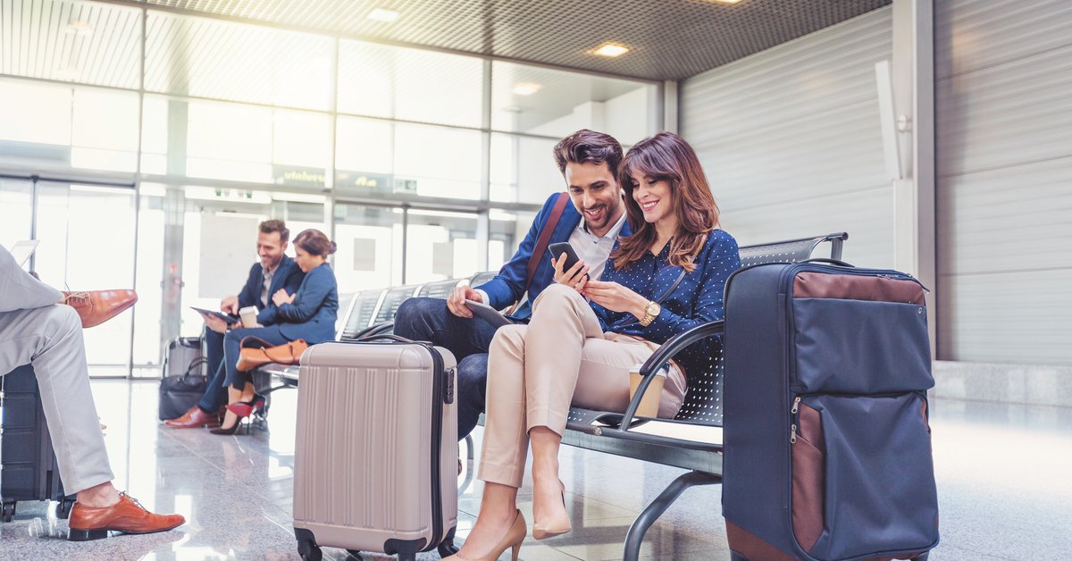 Smiling couple looks at phone together while waiting with luggage in airport