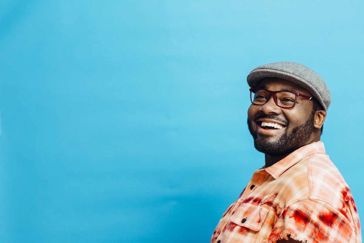 A smiling man standing in front of a bright blue wall.