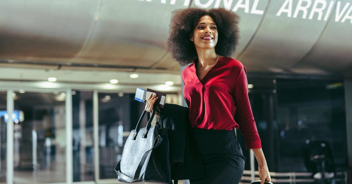 Smiling traveler walks through airport with luggage in tow.