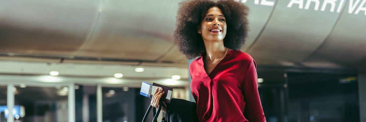 Smiling traveler walks through airport with luggage in tow.