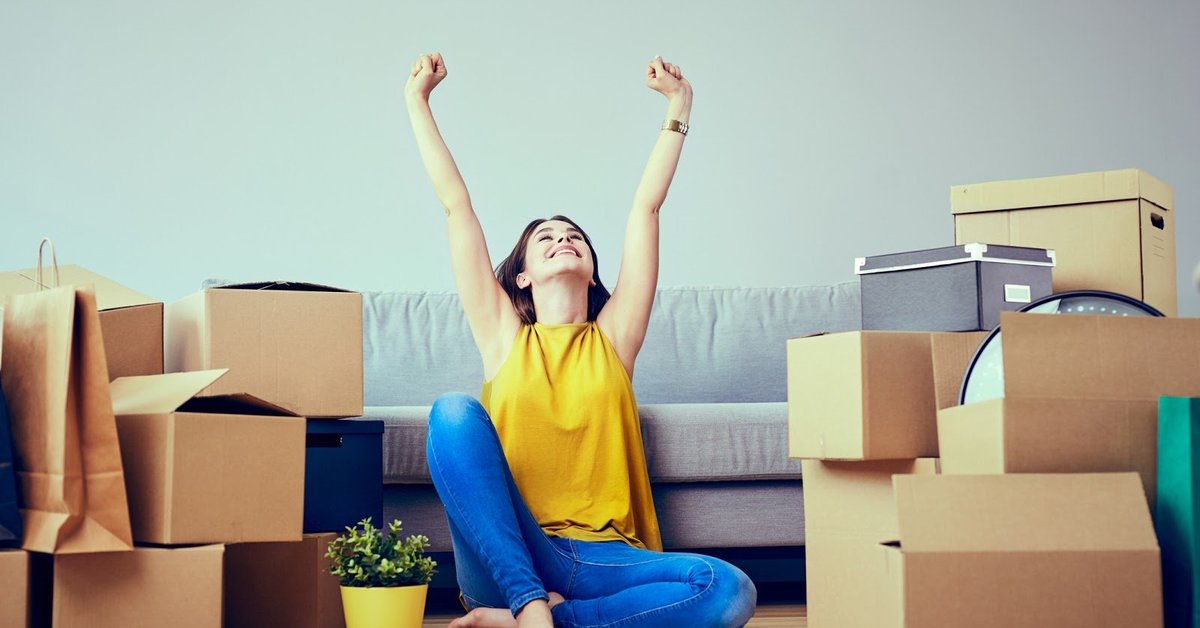 Happy Young Woman Sitting In New Home Between Stacks Of Boxes