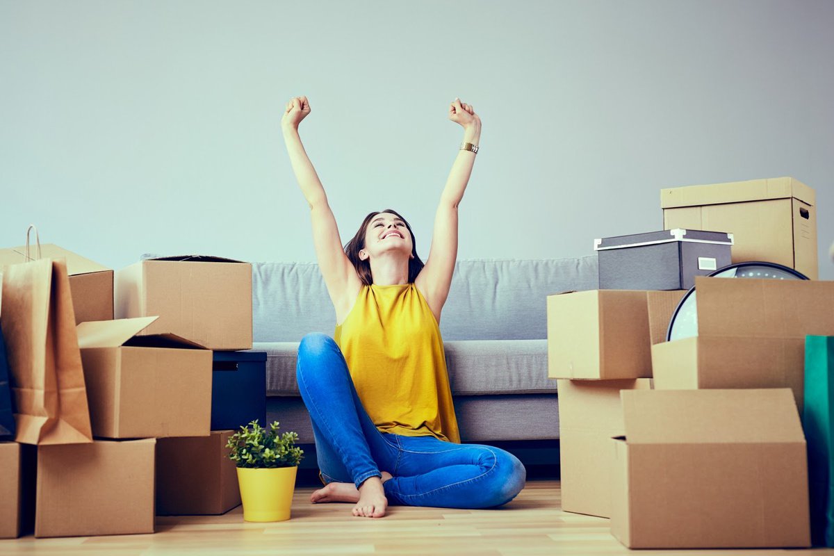 Happy Young Woman Sitting In New Home Between Stacks Of Boxes