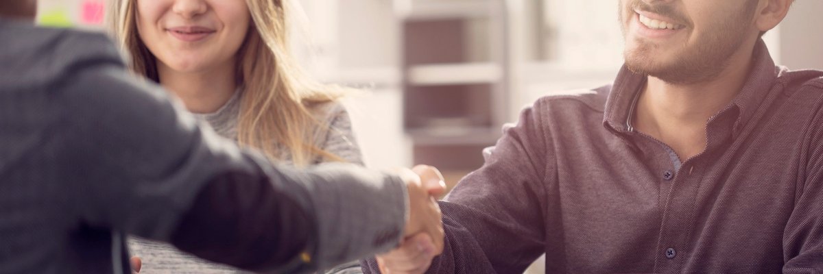 A smiling young couple shaking hands with someone over a desk.
