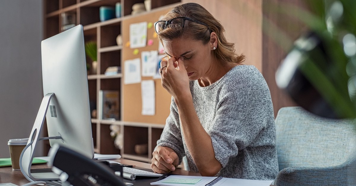A stressed businesswoman sitting at her computer with her hand on her face.