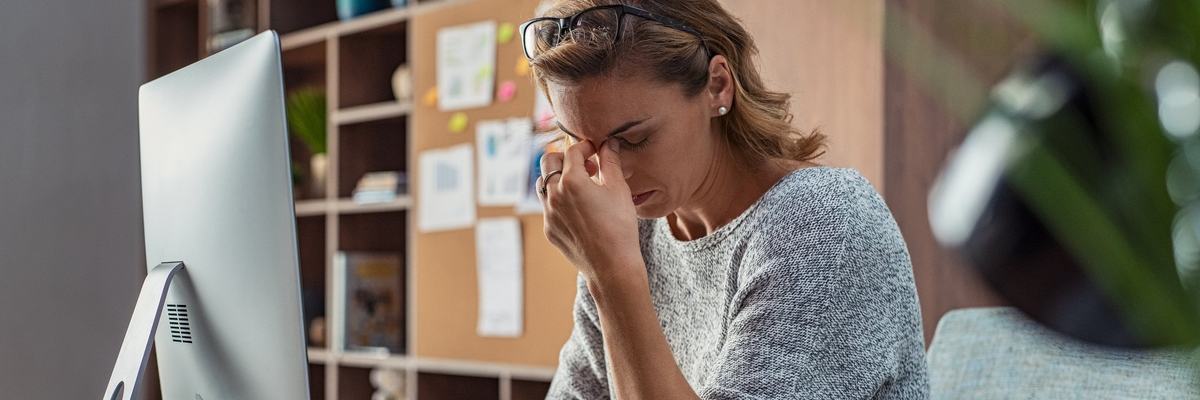 A stressed businesswoman sitting at her computer with her hand on her face.