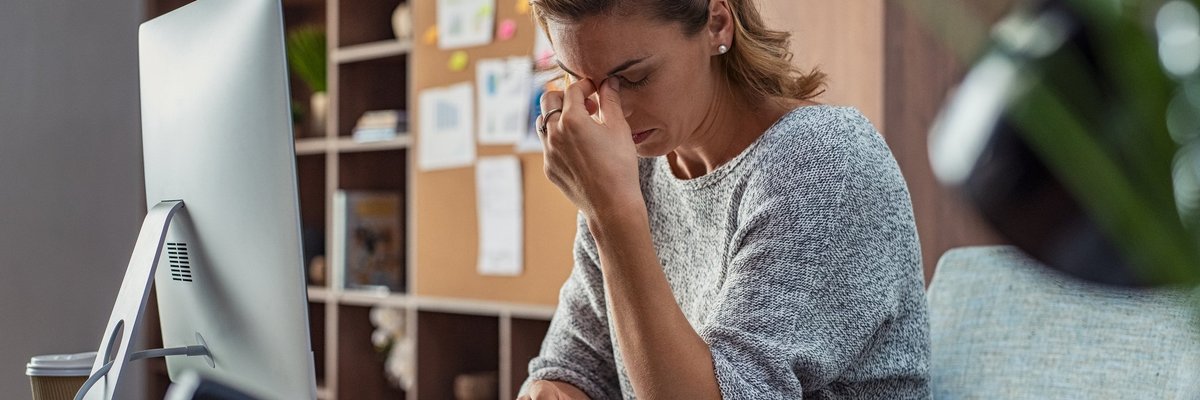 A stressed businesswoman sitting at her computer with her hand on her face.