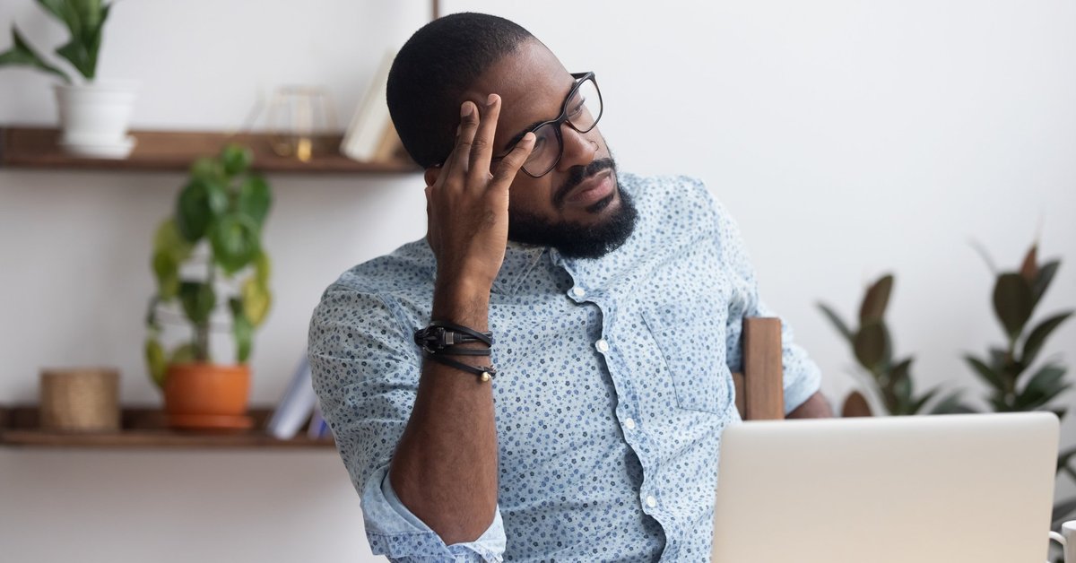 A stressed man sitting at a desk with his hand on his forehead.