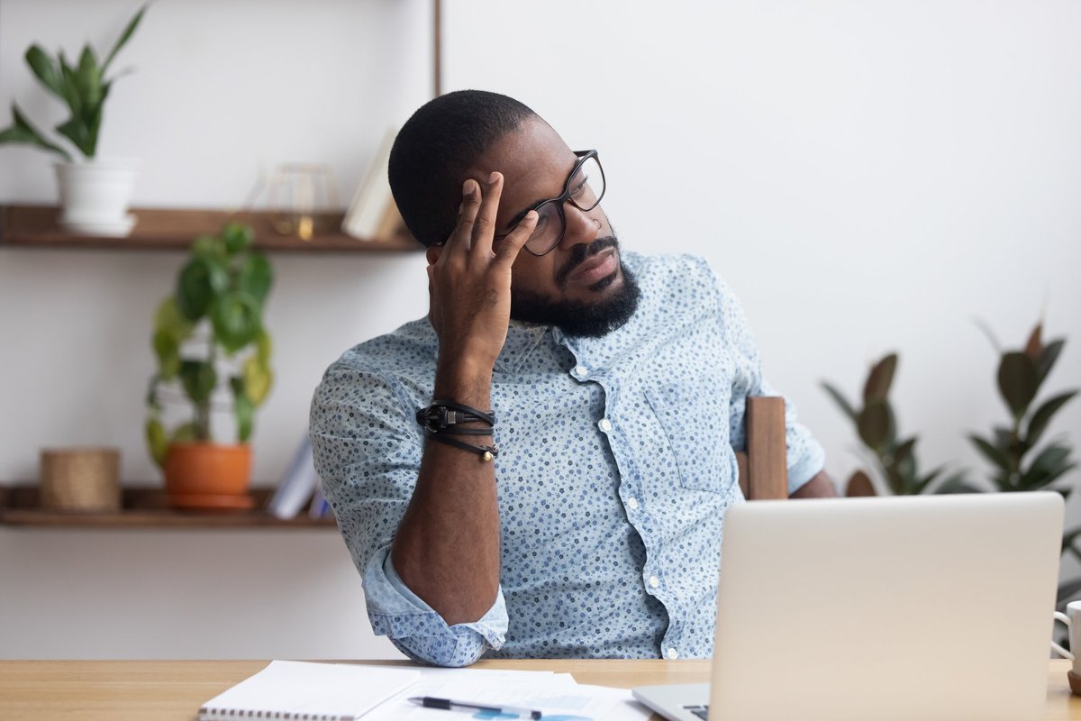 A stressed man sitting at a desk with his hand on his forehead.