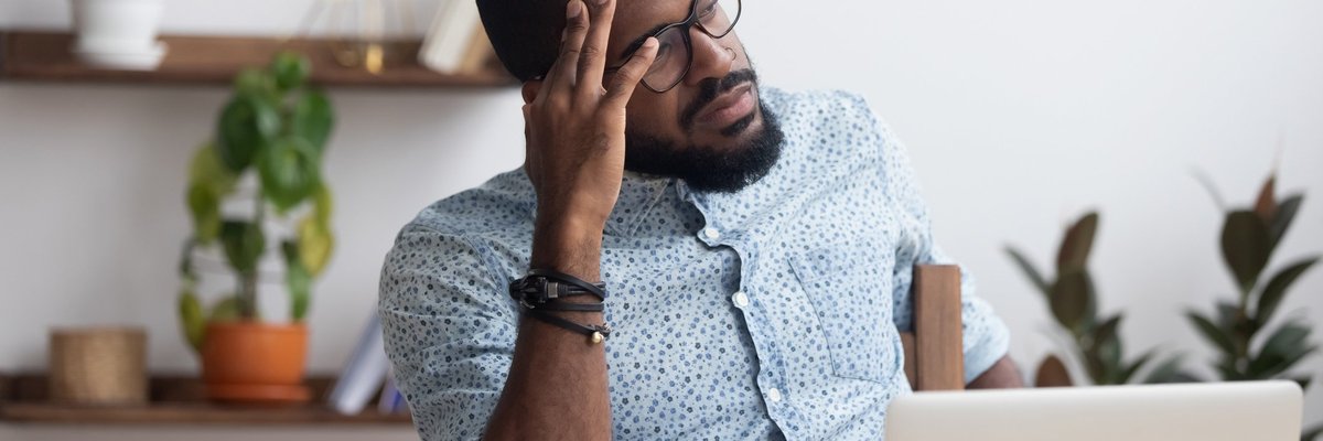 A stressed man sitting at a desk with his hand on his forehead.