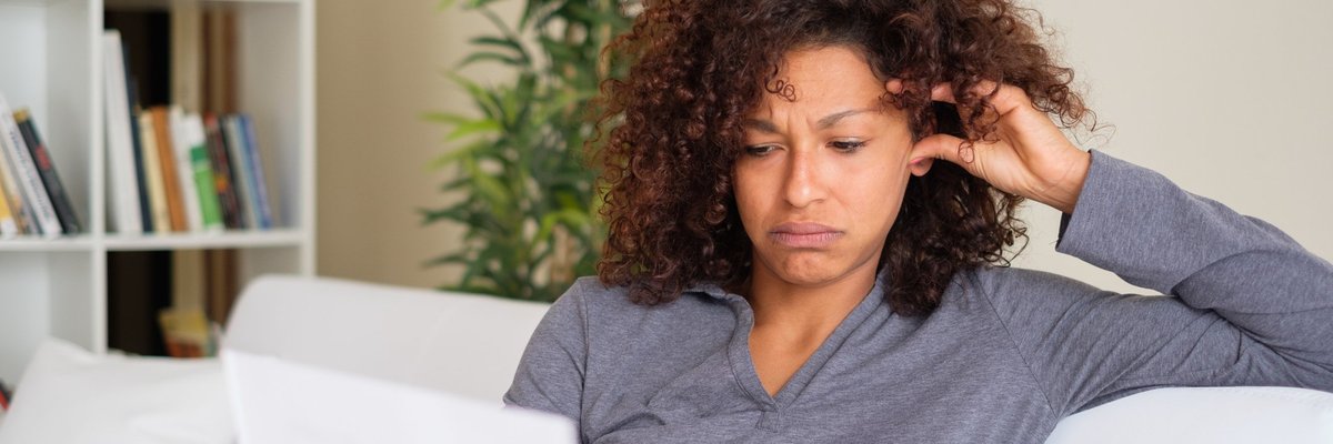 A stressed woman reading paperwork while sitting on her couch.