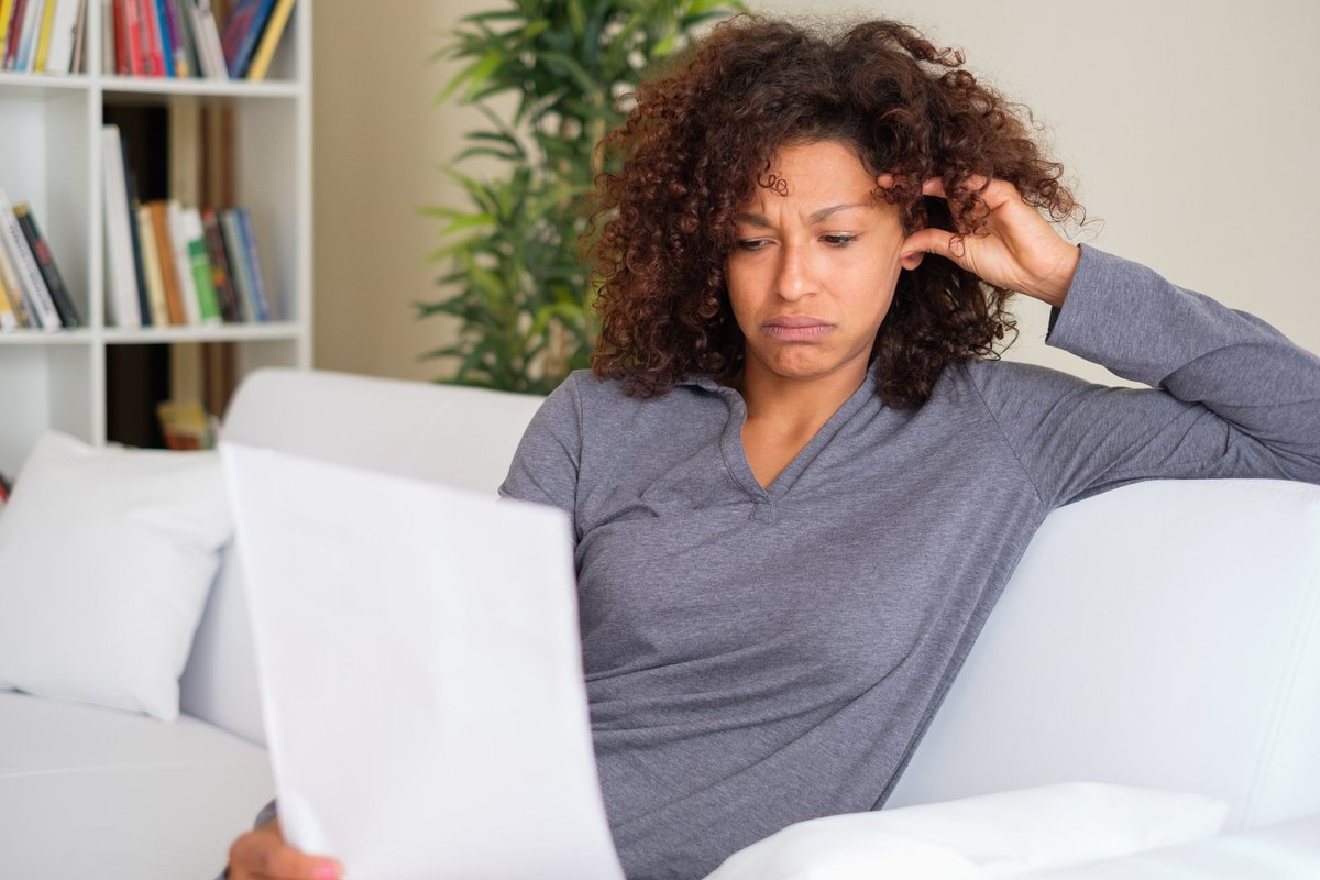 A stressed woman reading paperwork while sitting on her couch.