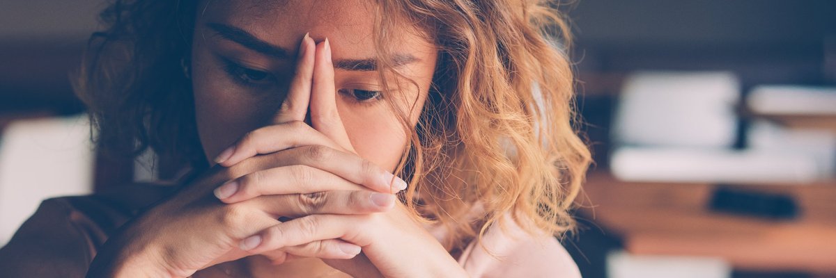 A stressed young woman sitting with her hands covering her face.