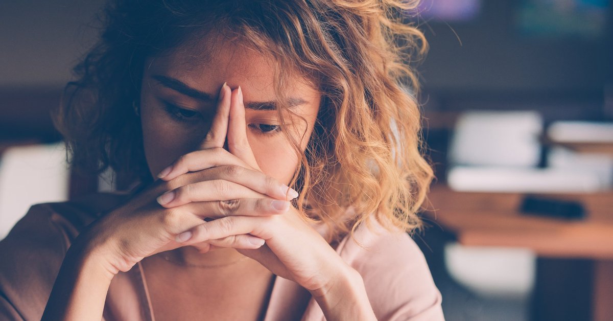 A stressed young woman sitting with her hands covering her face.