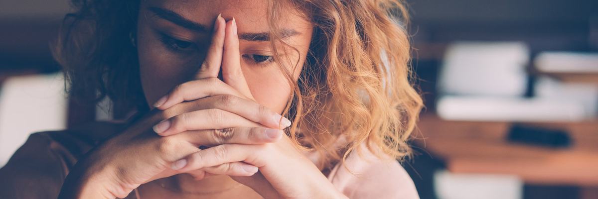 A stressed young woman sitting with her hands covering her face.