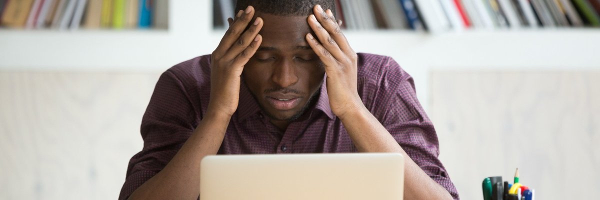 A person holding his head in his hands while looking disappointed at his laptop.
