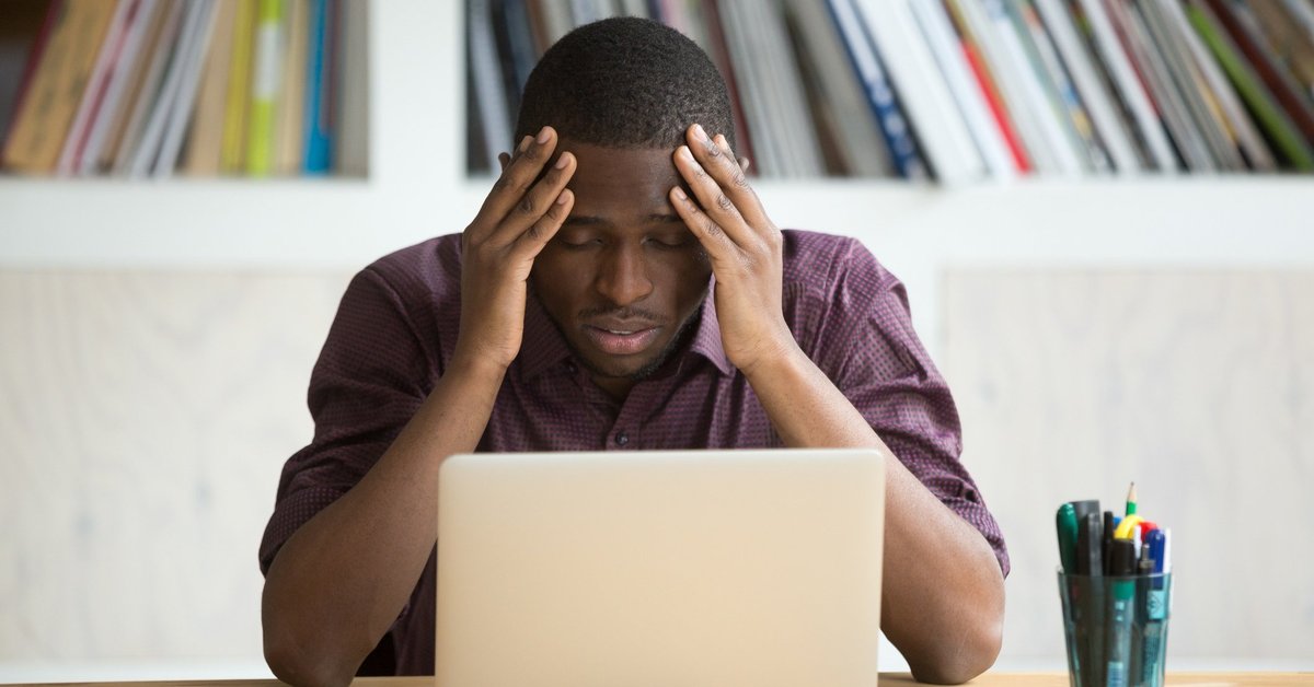 A person holding his head in his hands while looking disappointed at his laptop.