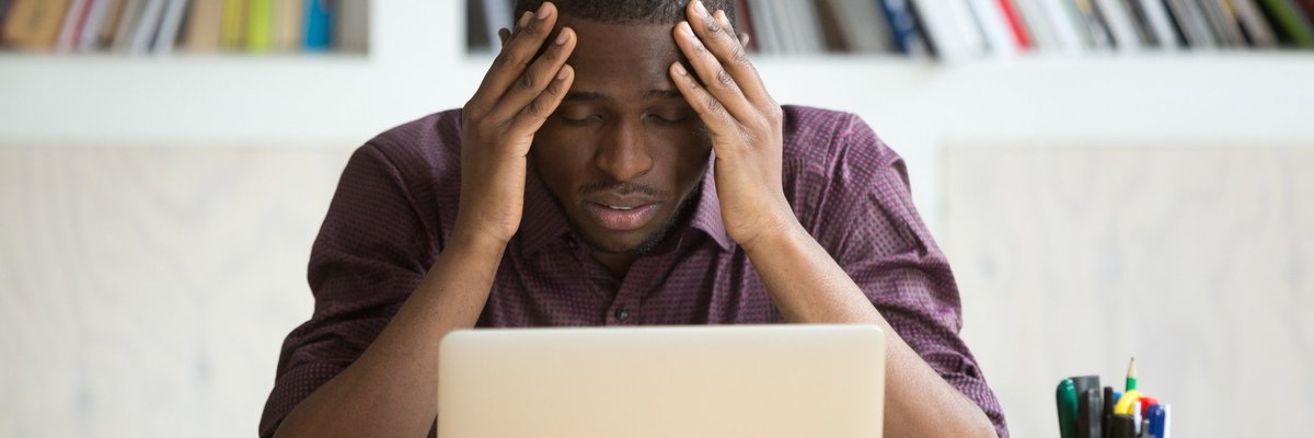 A person holding his head in his hands while looking disappointed at his laptop.